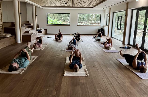 A quiet yoga room with several people lying on mats. The gentle lighting creates a relaxing atmosphere.