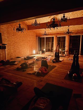 Ein ruhiger Yoga-Raum mit dimmendem Licht. Teilnehmer praktizieren verschiedene Positionen auf Yogamatten.
