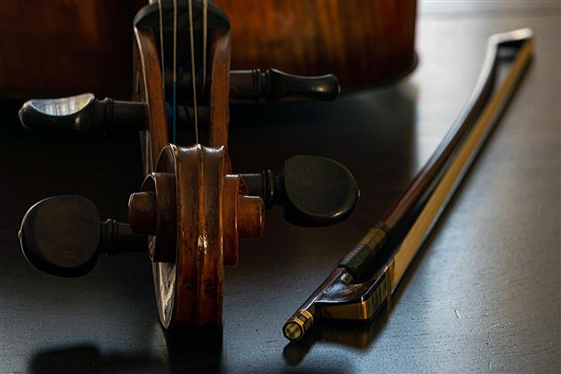 Eine Violine mit einem gefärbten Holzgriff und einem Bogen liegen auf einem Tisch. Die Instrumente sind auf einem dunklen Hintergrund gut sichtbar.