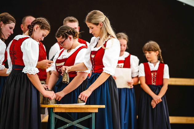 Eine Gruppe von Menschen in traditionellen Trachten steht um einen Tisch. Einige von ihnen scheinen an einer Aktivität oder Zeremonie teilzunehmen.