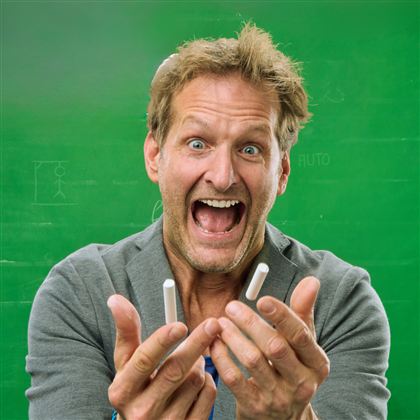 Ein Mann mit freudigem Gesichtsausdruck hält zwei Stifte in den Händen. Der Hintergrund ist eine grüne Tafel.