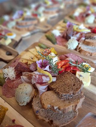 Een aantrekkelijk kaas- en vleesplank met verschillende broden en verse ingrediënten. Kleurrijke bloemen en kruiden geven de schikking extra charme.