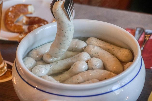 En skål med hvidwurst, der svømmer i varmt vand. Ved siden af ligger et stykke pretzel.