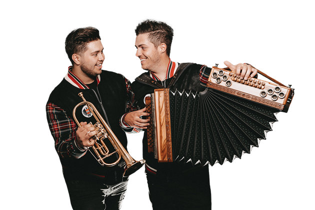 Two musicians stand together and smile. One holds a trumpet, the other an accordion.