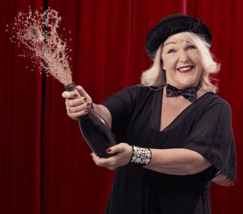 A laughing woman is sitting on a brown sofa. She has red hair and is wearing a white dress.