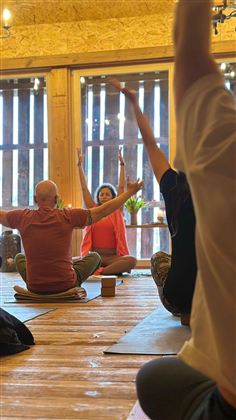 Eine Gruppe von Menschen praktiziert Yoga in einem hellen Raum. Die Atmosphäre ist ruhig und entspannt, mit Holzwänden und natürlichem Licht.
