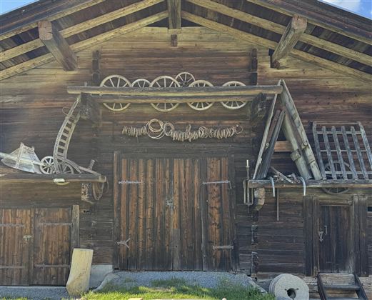 Eine rustikale Holzhütte mit traditionellen Elementen und einer grünen Wiese davor. Der Himmel ist blau mit wenigen Wolken.