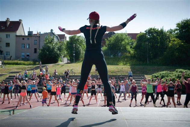 Eine Gruppe von Menschen macht Sport unter der Anleitung einer Trainerin. Sie zeigen verschiedene Fitnessübungen an einem sonnigen Tag im Freien.