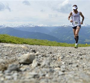 Ein Läufer meistert einen Bergweg mit Blick auf schneebedeckte Berge. Die Mischung aus Natur und Aktivität vermittelt ein Gefühl von Abenteuer.