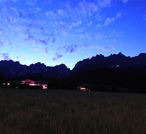 A breathtaking mountain landscape at dusk, with a shimmering silhouette of the mountains. The sky is clear and tinted in soft shades of blue and violet.