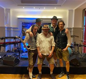 Eine Band steht auf der Bühne, umgeben von Musikinstrumenten. Sie tragen traditionelle Kleidung und posieren für das Foto.