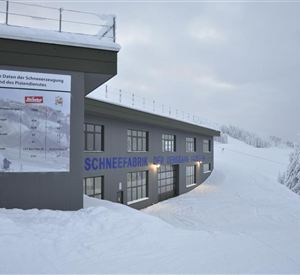 A modern building in a snowy landscape. Signs with technical information about snow production are visible.