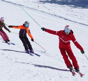 Three skiers are riding in a snowman under a sunny sky. They are wearing colorful ski clothes and enjoying winter sports.