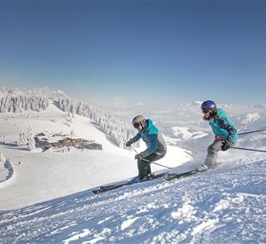 Two skiers are skiing down a snowy slope. In the background, a picturesque winter landscape can be seen.