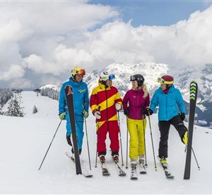 A group of four skiers is standing on a snow-covered slope. In the background, there are mountains and a cloudy sky.