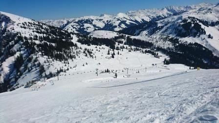 A snow-covered mountain landscape with many fir trees. Ski activities and mountain peaks are visible in the background.