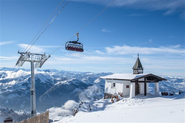 Eine schneebedeckte Berglandschaft mit einer Seilbahn und einem kleinen Gebäude. Der Himmel ist klar und blau, mit beeindruckenden Bergen im Hintergrund.