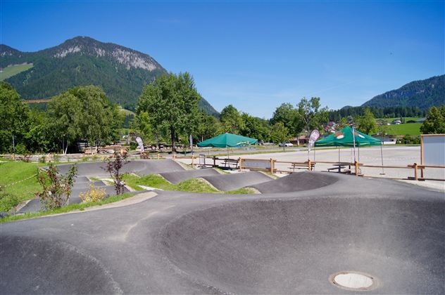 Eine moderne Skate-Anlage mit geschwungenen Rampen und einer schönen Berglandschaft im Hintergrund. Die Umgebung ist grün und einladend, ideal für Outdoor-Aktivitäten.