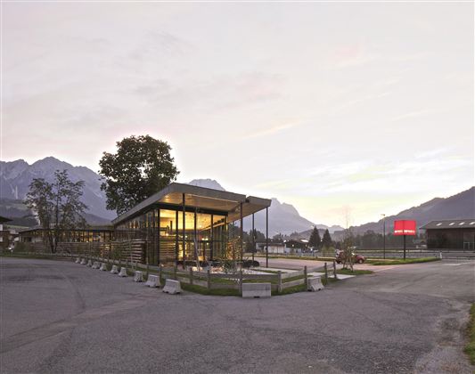 Een modern gebouw met glazen façade in een bergachtige omgeving. De zachte avondstemming en de omringende bergen creëren een uitnodigende sfeer.