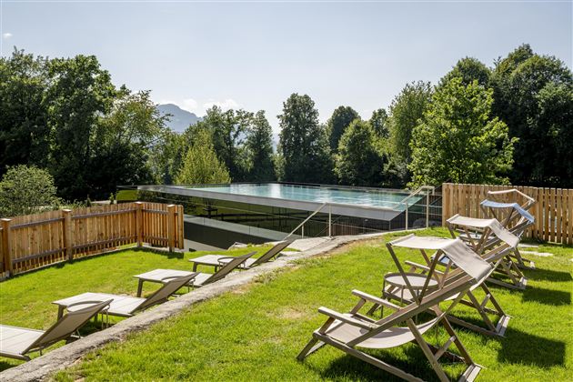 A beautiful outdoor area with loungers and a modern pool.  
Surrounded by lush greenery and trees.
