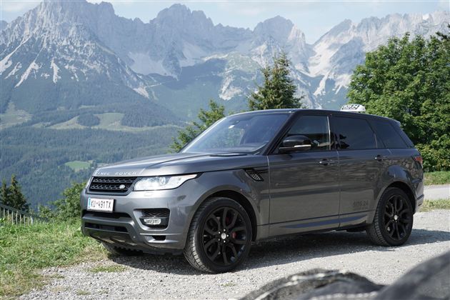 Ein eleganter SUV steht auf einem Schotterweg vor einer beeindruckenden Berglandschaft. Die malerischen Berge und der klare Himmel verleihen der Szene eine majestätische Atmosphäre.
