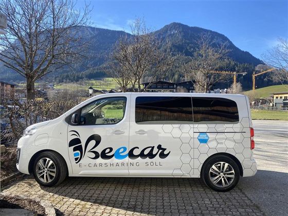 An e-carsharing vehicle of the brand Beecar is standing at the edge of a road. In the background, mountains and a clear sky are visible.