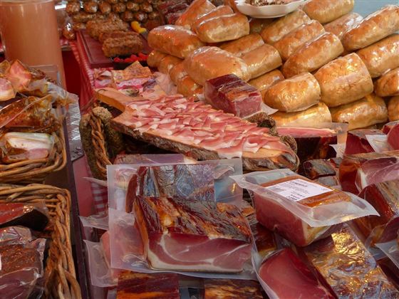A market table with various sausage and meat products. In the background, many bread rolls can be seen.