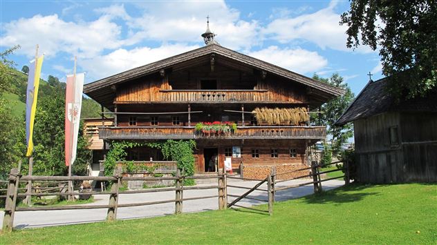 Ein traditionelles Holzhaus mit Balkonen und Blumen. Der Garten ist grün und ein Zaun umgibt das Grundstück.