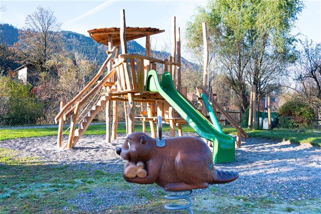 A playground with a large wooden slide and a slide mountain. In front of the slide, there is a playful, brown animal.