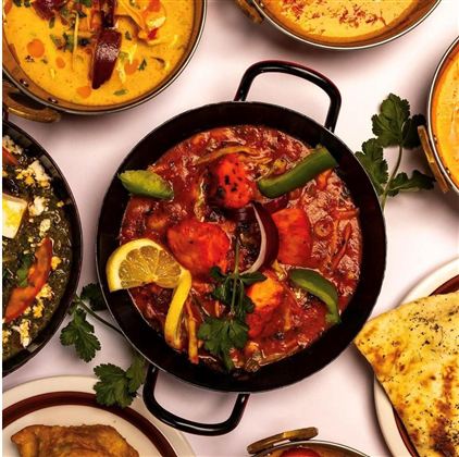 Delicious Indian food with various curries and side dishes. The main dish in the center contains chicken and fresh vegetables.