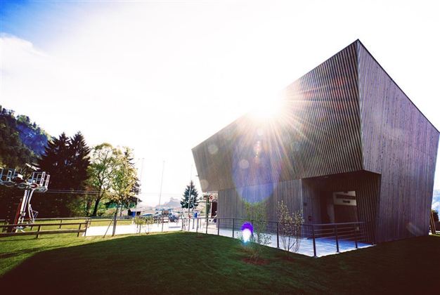 Een modern houten gebouw met een opvallend ontwerp. De zon schijnt fel en zorgt voor een fijne sfeer buiten.