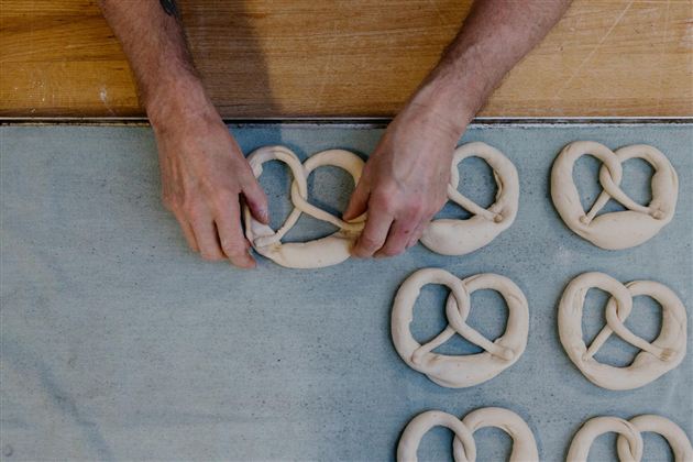 Een bakker vormt pretzels van deeg. De pretzels liggen op een bakplaat.