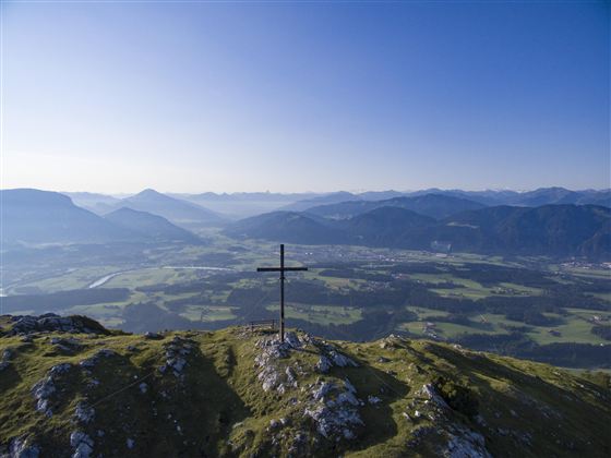 Een mooi huis op een weiland, omringd door kleurige bloemen en groene heuvels. De lucht is blauw met enkele witte wolken.