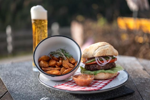 A juicy hamburger with fresh vegetables on a plate. Accompanied by crispy potato pieces and a beer in a glass.
