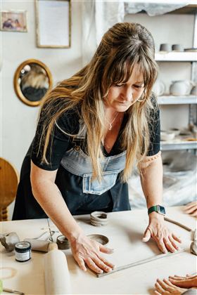 Eine Frau arbeitet konzentriert am Tisch mit Ton. Sie formt kreativ Kunstwerke in einer hellen Werkstatt.