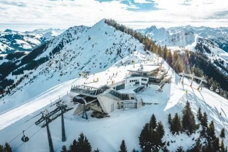 A picturesque mountain landscape with snow-covered peaks. In the foreground, a mountain station and chairlifts can be seen.