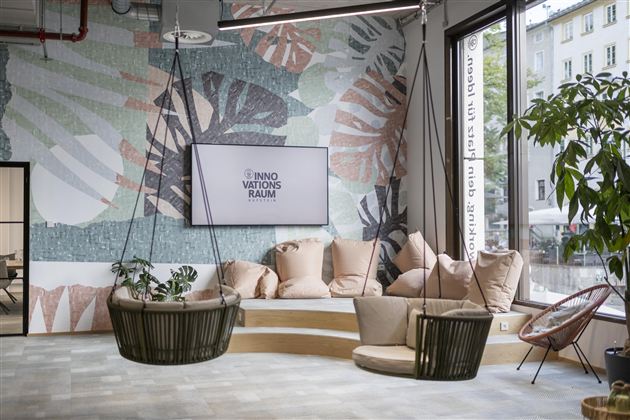 A modern room with a large wall design of leaves. There are comfortable seating areas and swing chairs that create an inviting atmosphere.