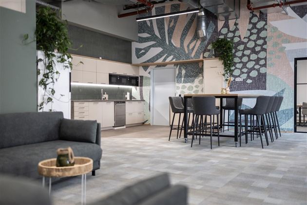 A modern office kitchenette with a large table and chairs. The walls are decorated with colorful, floral patterns.