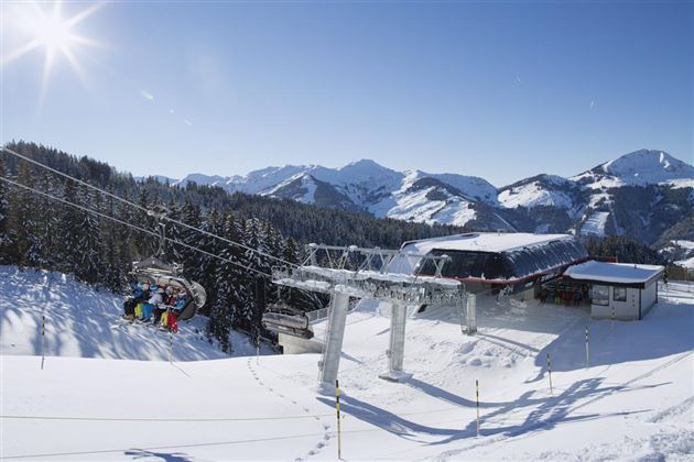 A wintry mountain landscape with snow-covered mountains and a gondola. The sky is clear and sunny.
