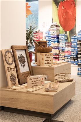 A sales display with decorative wooden objects stands in the foreground. In the background, shelves with colored shoe boxes are visible.