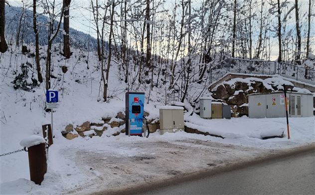 Ein Parkplatz in einer verschneiten Landschaft mit Bäumen. Im Vordergrund steht ein Parkautomaten.