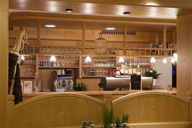 Een stijlvolle houten bar met veel glazen en dranken. De gezellige sfeer wordt accentueert door zachte verlichting en planten.