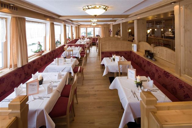 Een elegant restaurant met witte tafelkleden en houten interieur. Grote ramen zorgen voor veel daglicht en een uitnodigende sfeer.