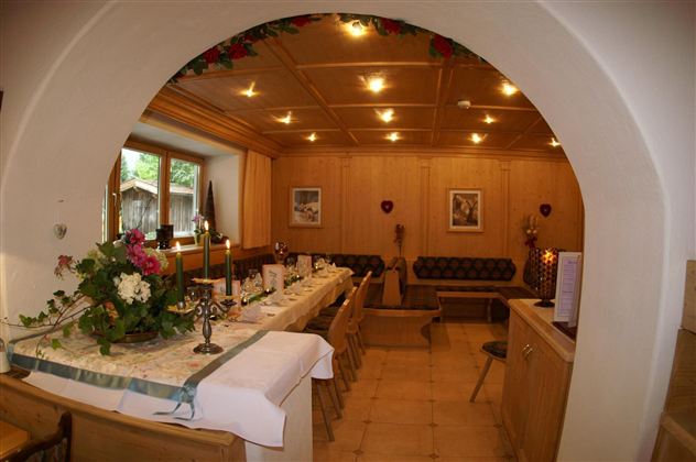 Een gezellige ruimte met een lange tafel, versierd met bloemen en kaarsen. De wanden zijn van hout, en er zijn comfortabele zitplaatsen langs de wanden.