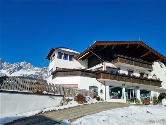 Ein charmantes alpenländisches Haus mit mehreren Etagen. Der Himmel ist klar und blau, und es liegt Schnee auf dem Boden.