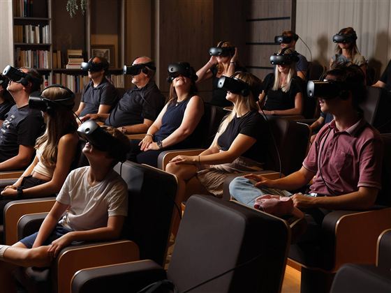 Eine Gruppe von Menschen trägt VR-Brillen und sitzt in bequemen Stühlen. Sie scheinen in ein virtuelles Erlebnis vertieft zu sein.