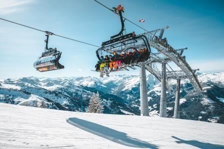 A cable car travels over snow-covered mountains. The sky is clear and sunny.
