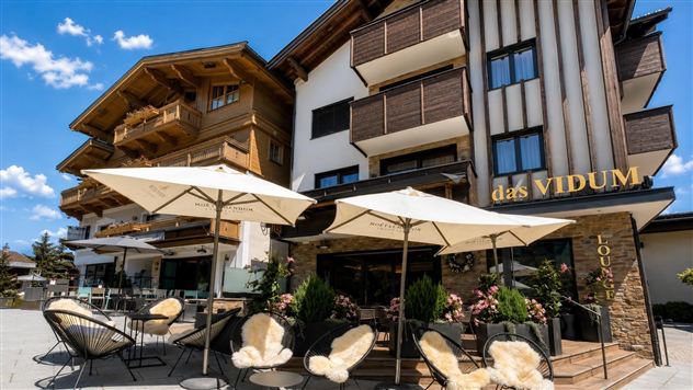 Ein modernes Hotel mit einem einladenden Außenbereich und Sonnenschirmen. Die Architektur kombiniert Holz- und Glaselemente und vermittelt eine gemütliche Atmosphäre.