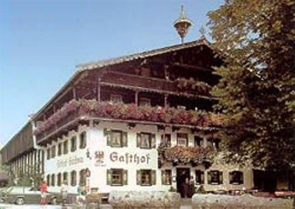 A traditional inn with blooming balconies and a cozy atmosphere. The surroundings are characterized by trees and a clear view.