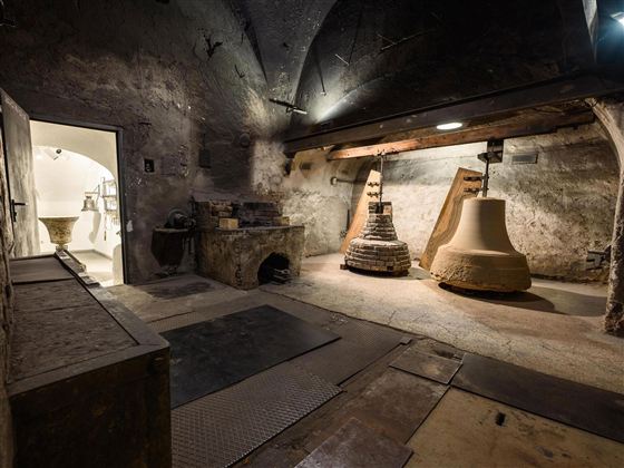Ein historischer Glockenturm mit zwei großen Glocken. Der Raum hat eine rustikale, steinerne Atmosphäre und eine Tür, die zu einem weiteren Bereich führt.